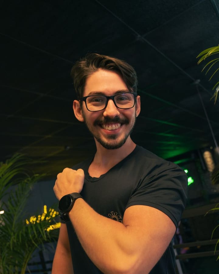 Caio Gatti, personal trainer em Bauru, sorrindo e mostrando o braço na academia